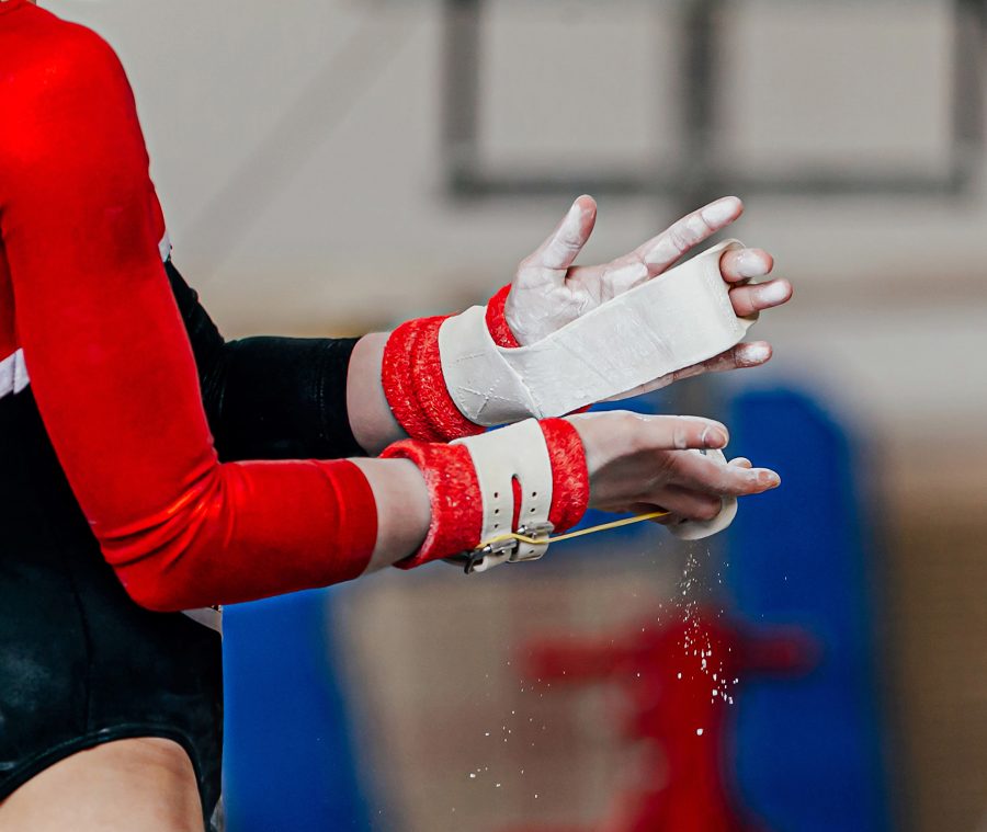 close-up hands female gymnast in gymnastics grips in gym chalk, uneven bars performing